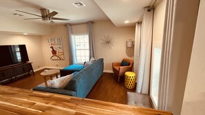 Un salon moderne avec un canapé bleu, une table basse en bois, un téléviseur et un ventilateur de plafond.