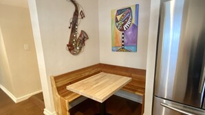 Une cuisine compacte avec un banc en bois, un réfrigérateur en acier inoxydable, un tableau abstrait aux couleurs vives et un saxophone accroché au mur.