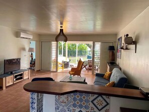 A living room with a TV, sofa, and a dining area with chairs and a table.