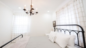 Une chambre à coucher avec un lit, un lustre, une fenêtre avec des rideaux et une horloge murale.