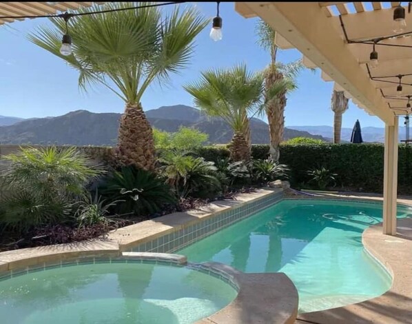 Relax by the serene pool surrounded by lush greenery and palm trees, with a mountain range in the background.