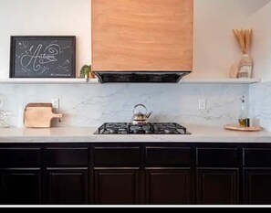 Enjoy cooking in this kitchen with a stainless steel gas stove, wooden cutting board, and utensil holder.