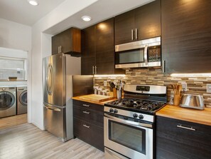 A modern kitchen with stainless steel appliances, dark wood cabinets, a wooden countertop, and a tiled backsplash. - Modern Mountain Home: Your Adventure Basecamp (Woodland Park)