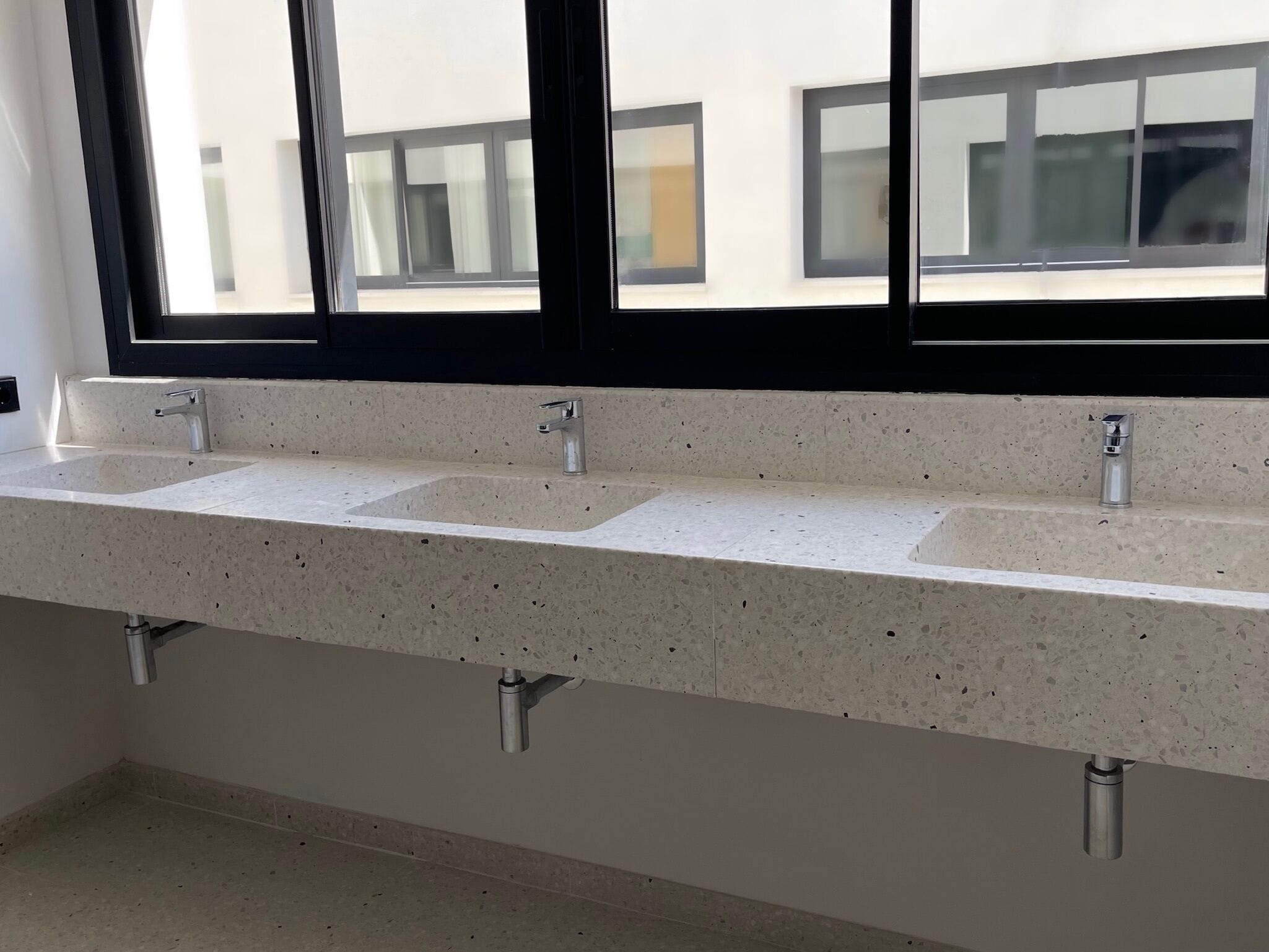 Une salle de bain avec trois lavabos, une fenêtre et une vue sur les bâtiments environnants.
