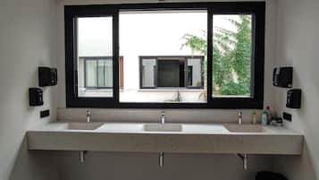 Un baño con dos lavamanos, un ventanal grande y un cubo de basura negro.