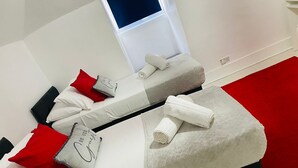 Un lit bien fait, avec des oreillers blancs et rouges, une serviette blanche et un tapis rouge.