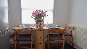 Un petit coin repas avec une table en bois et deux chaises, un vase de fleurs et un réfrigérateur sur le côté gauche.