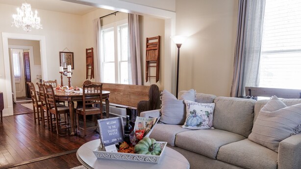 Een woonkamer met een eethoek, een bank, een salontafel met een schaal lekkernijen, en een kroonluchter.