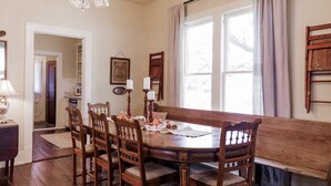 A dining room with a wooden table, chairs, a chandelier, and a view of the outdoors through a window. - The Church House – Historic Brenham Retreat (Brenham)
