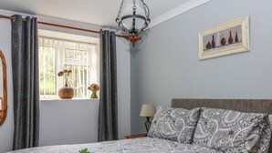Quarto com cama, janela com cortinas, abajur, quadro na parede e bandeja com chá sobre a cama.