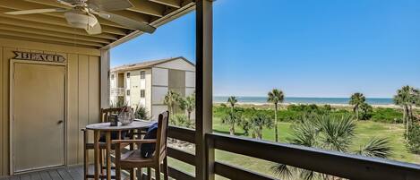 A covered outdoor area with a table and chairs, a ceiling fan, and a view of the beach and ocean.