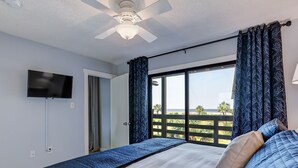 A bedroom with a bed, a ceiling fan, a TV, and a view of the beach. - Ocean Views with Easy access to pools and beach (Tybee Island)