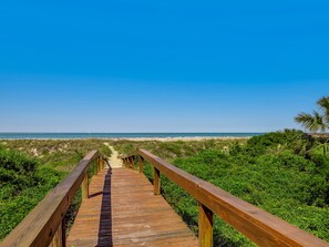 Ein Holzsteg führt zu einem Strand unter blauem Himmel.