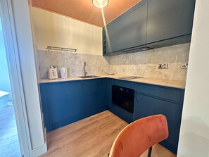 A compact kitchen with dark blue cabinets, a built-in dishwasher, and a marble countertop.
