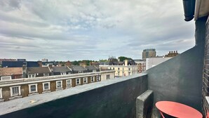 En takterrass med ett rött, hopfällbart bord, med utsikt över en rad byggnader med varierande arkitektur.