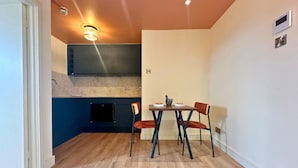 Ett kompakt kök med mörkblå skåp, en svart ugn och en matplats med två stolar och ett litet bord.