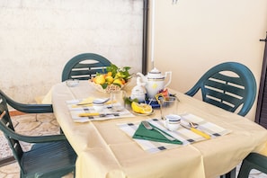 A table set with a tablecloth, chairs, a fruit basket, a teapot, cups, and cutlery.