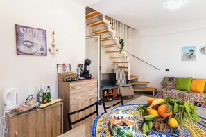 Une pièce avec un escalier, un canapé, une table avec des fruits, un coin café et une télévision.