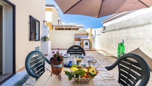 Un patio con mesa lista para comer, sillas exteriores, un gran paraguas y una lavadora al fondo.
