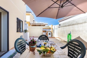 Eine Terrasse mit Esstisch, Gartenstühlen, einem großen Sonnenschirm und einer Waschmaschine im Hintergrund.