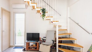 Una escalera con escalones de madera y barandillas blancas, un televisor sobre un soporte de madera, una silla a rayas y un pequeño estante con adornos.