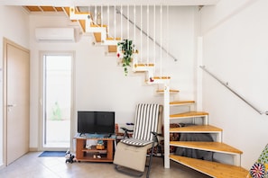A staircase with wooden steps and white railings, a television on a wooden stand, a striped chair, and a small shelf with decorative items.