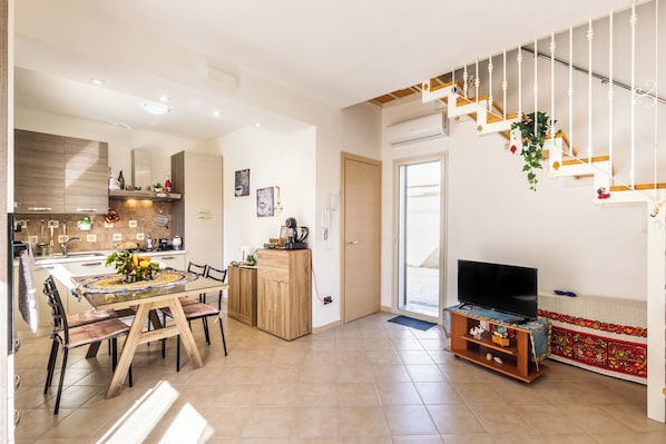 A modern kitchen with a dining area, a staircase, and a TV in a living room.