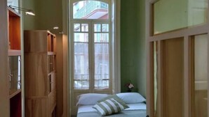 A bedroom with a checkered floor, a bed with striped bedding, and a window with a view of buildings.