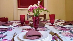 A dining table set with red glassware, a floral tablecloth, and a vase with pink flowers.