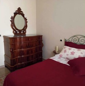 A bedroom with a wooden dresser, a bed with a floral bedspread, and a nightstand with a candle.
