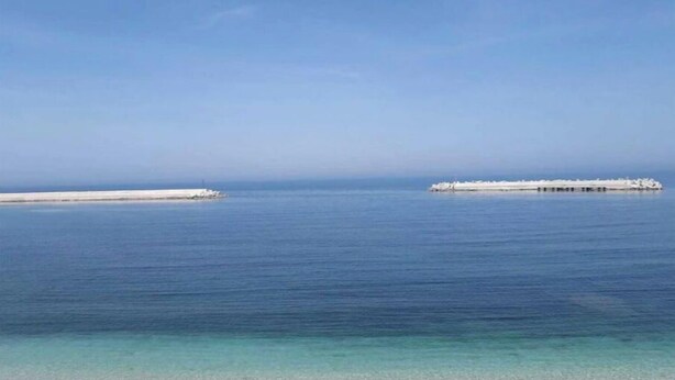 A beach with clear blue water and a sandy shore.