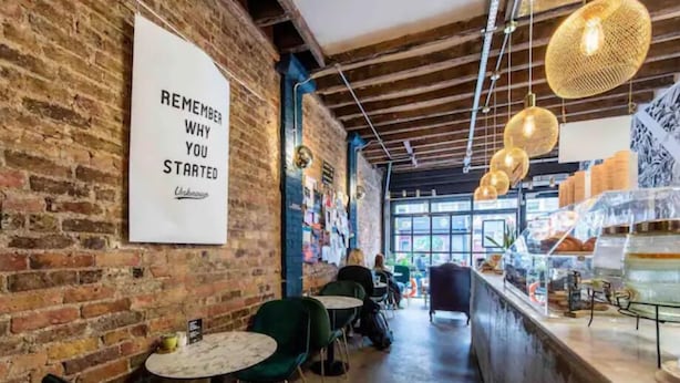 Un accogliente caffè con pareti in mattoni a vista, un cartello che invita i clienti a ricordare il motivo per cui hanno iniziato, e un bancone con diversi articoli in mostra.