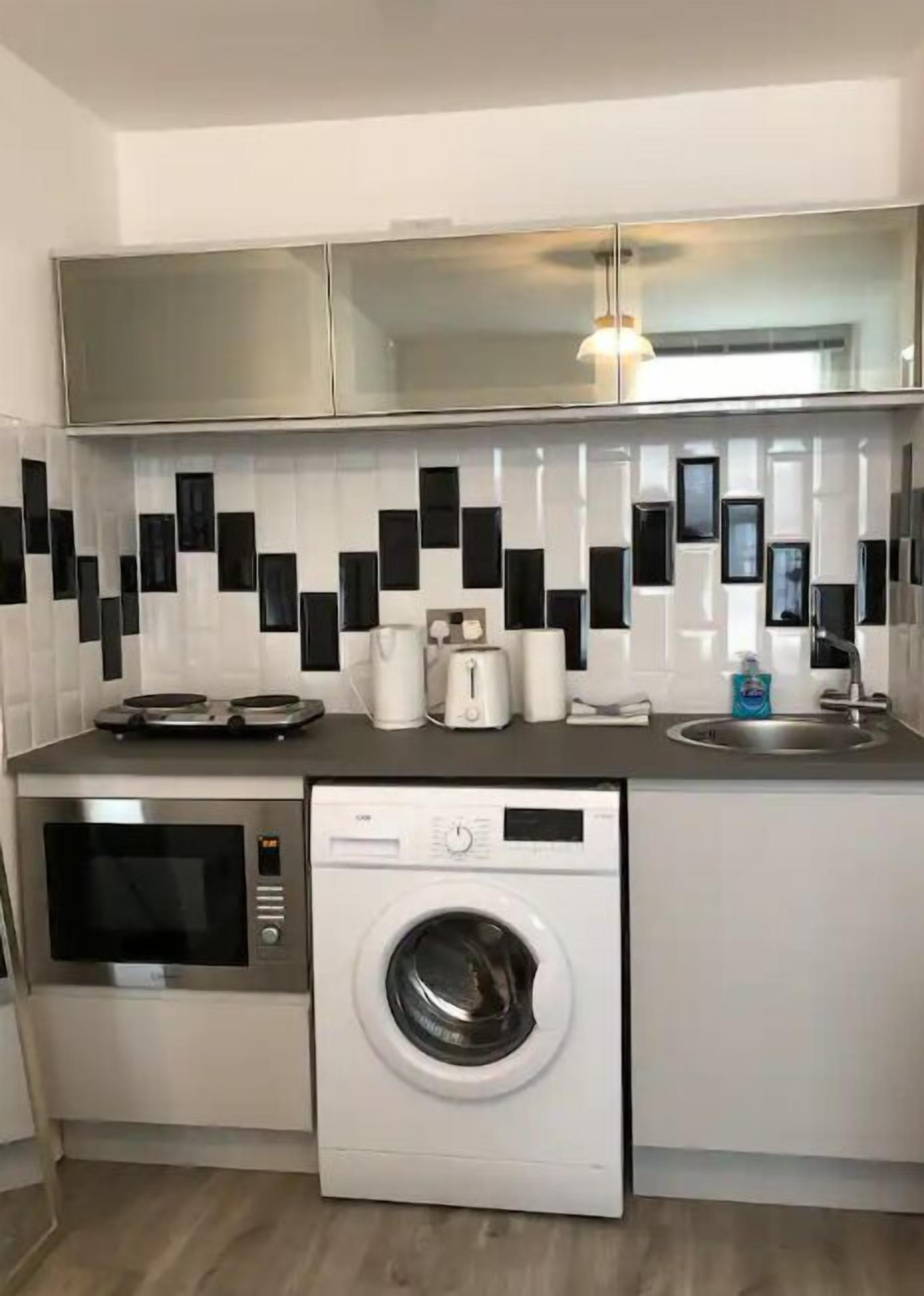 A compact kitchen with a washing machine, microwave, and a sink.