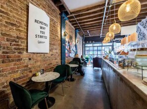 Un café chaleureux aux murs en briques apparentes, avec une pancarte encourageant les clients à se remémorer les raisons qui les ont motivés à se lancer, et un comptoir où sont exposés divers articles.
