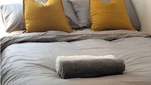 Een net opgemaakt bed met grijze beddengoed en twee mosterdgele kussens.