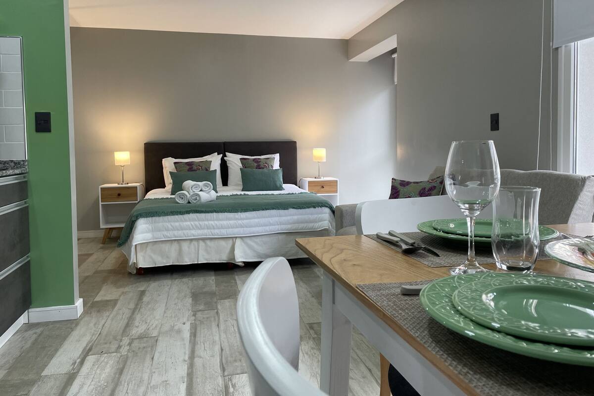 Une chambre d’hôtel moderne avec un lit, des tables de chevet, une table à manger avec des assiettes vertes et un verre d’eau.