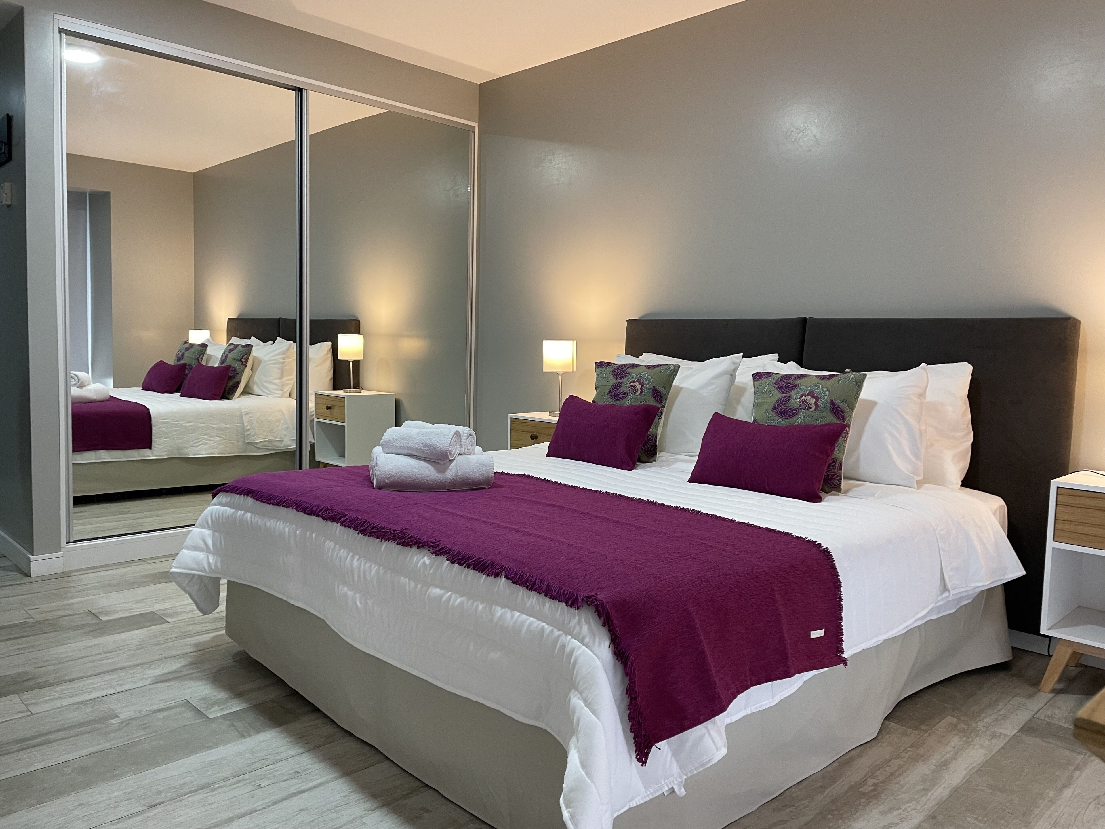 A modern hotel room with a large bed, a mirror, and two bedside tables.