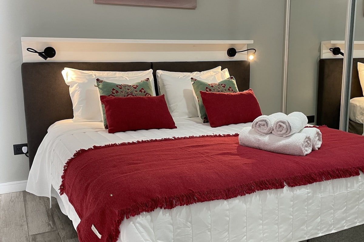 Une chambre à coucher moderne avec un grand lit, un plaid rouge et un lit bien fait, agrémenté de serviettes.