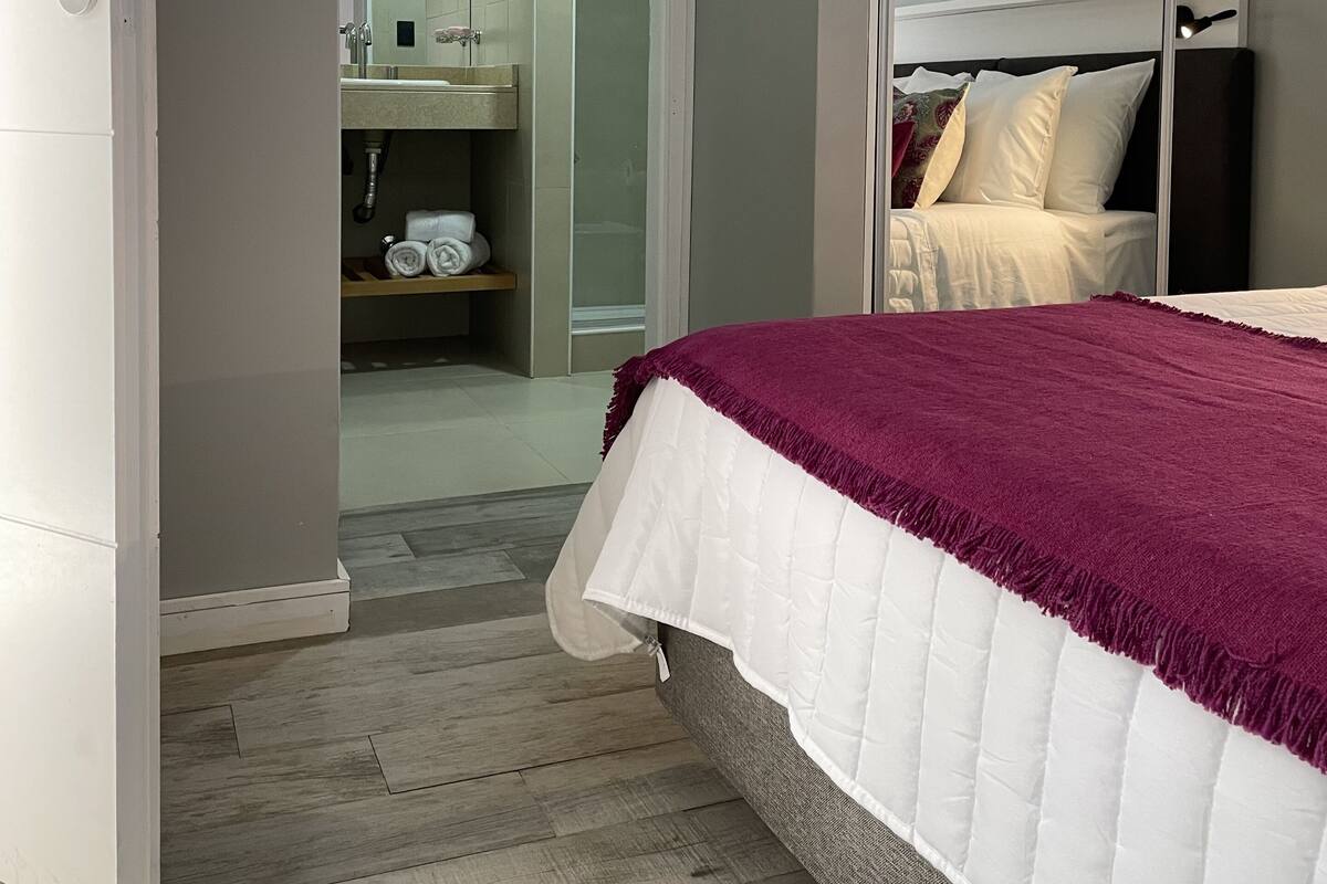 Une chambre à coucher avec un lit, une armoire et une salle de bain visible à travers une porte ouverte.