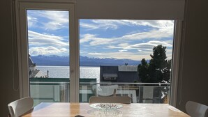 Een eetgedeelte met een tafel en stoelen, grote ramen met uitzicht op bergen en een meer.
