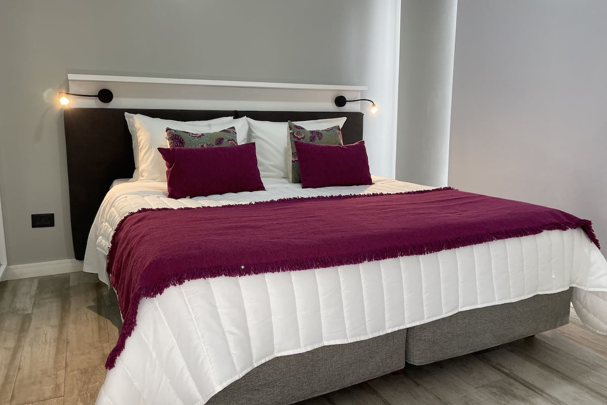 Un lit avec une couvre-lit blanche matelassée et un plaid violet, une tête de lit sombre et deux coussins décoratifs.