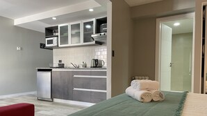 Een kleine hotelkamer met een kitchenette, een bed met een groene deken en een rode stoel.