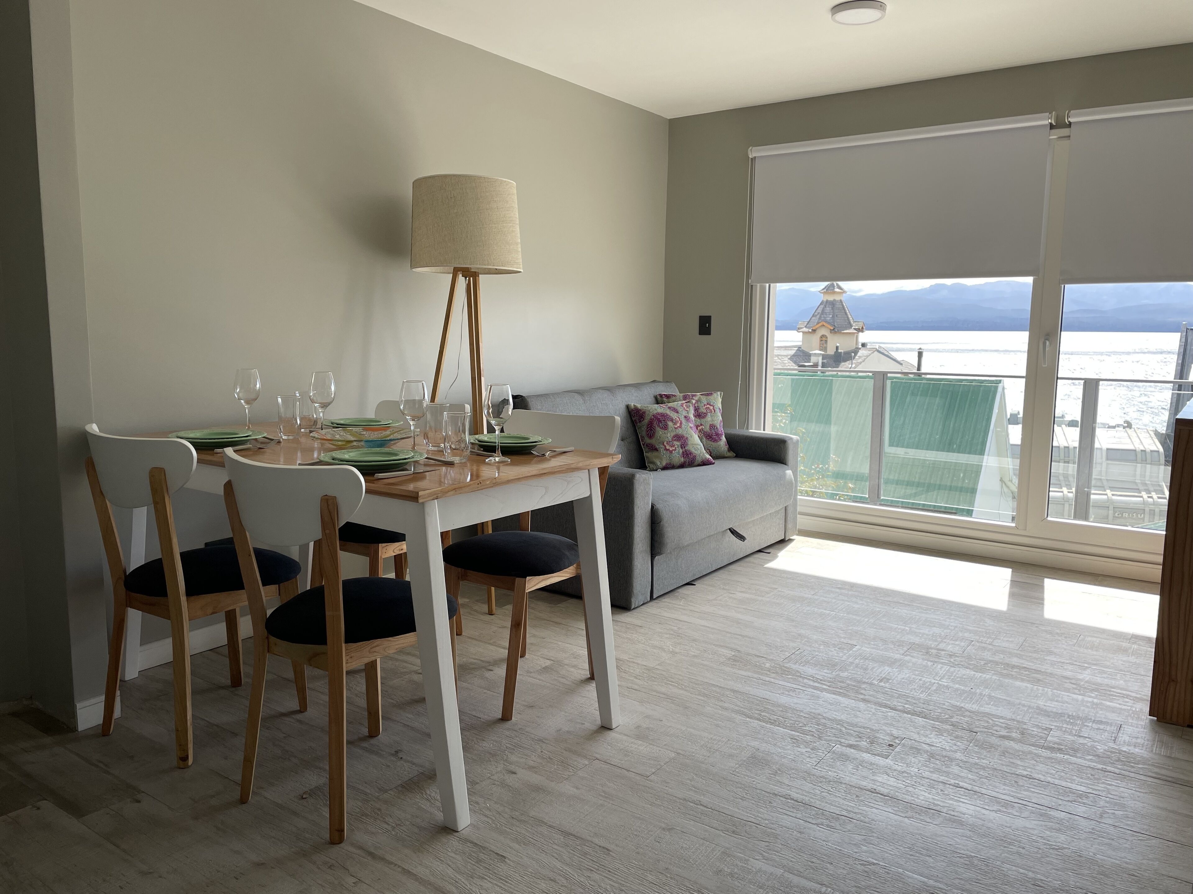 Een eethoek met een tafel gedekt voor vier personen, een bank en een groot raam met uitzicht op zee.