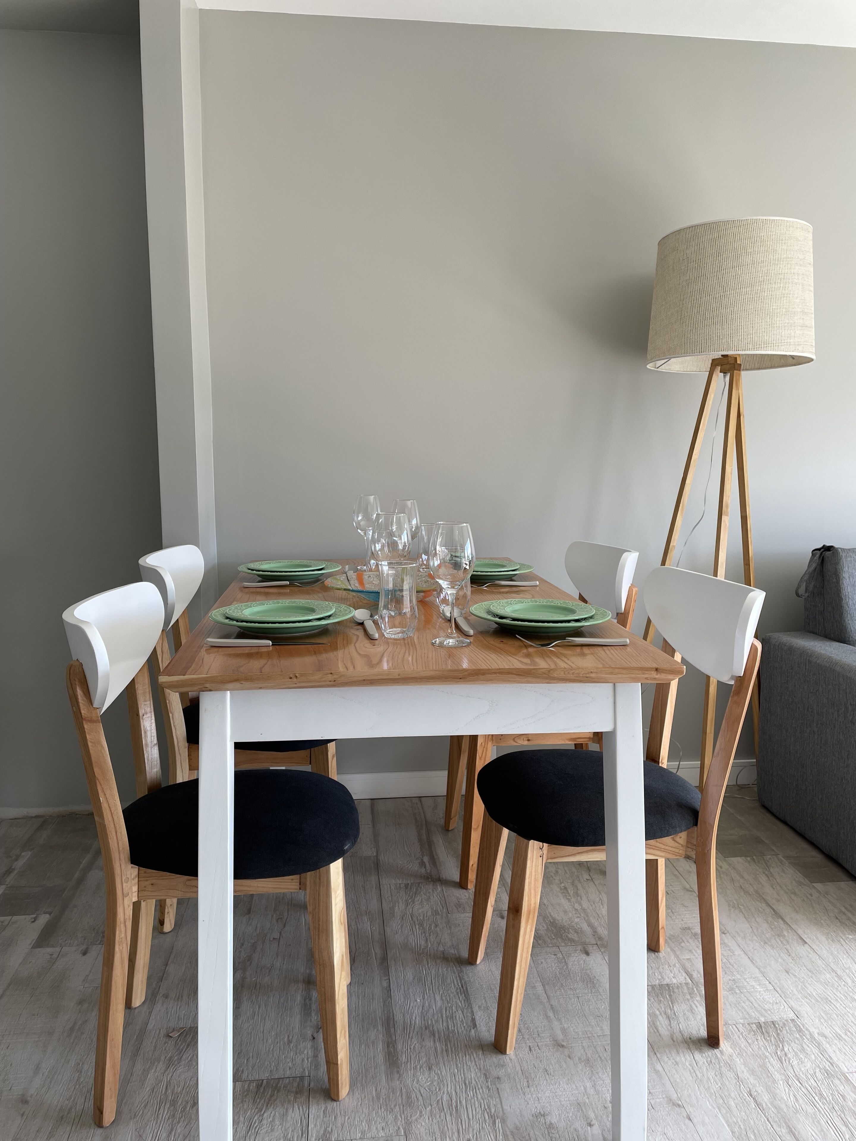 A dining table set with green plates, clear glasses, and a pitcher, surrounded by wooden chairs with black cushions.