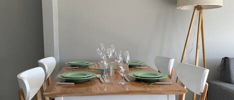 A dining table set with green plates, clear glasses, and a pitcher, surrounded by wooden chairs with black cushions.