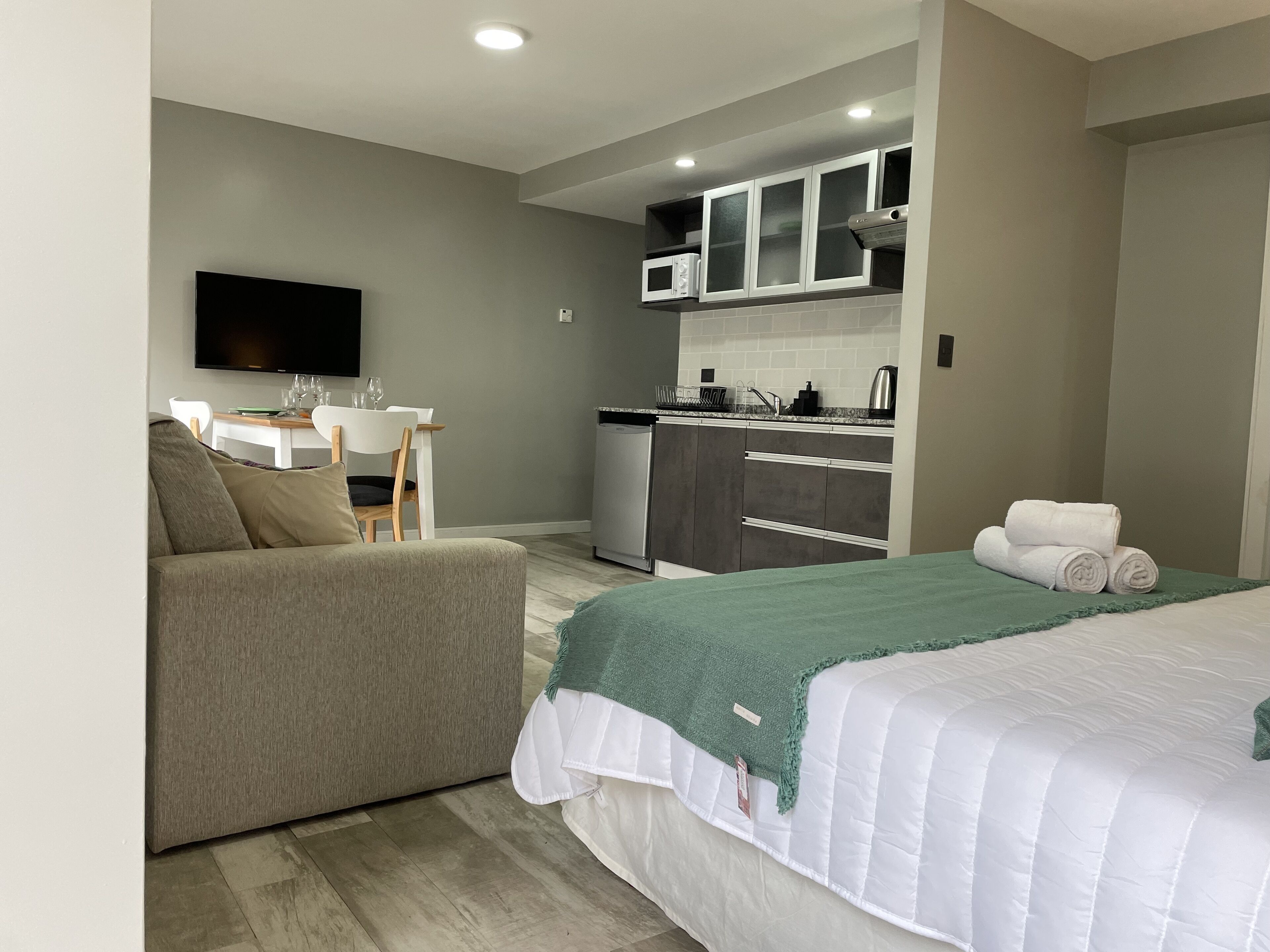 Een moderne hotelkamer met een bed, een slaapbank, een kleine kitchenette en een televisie.