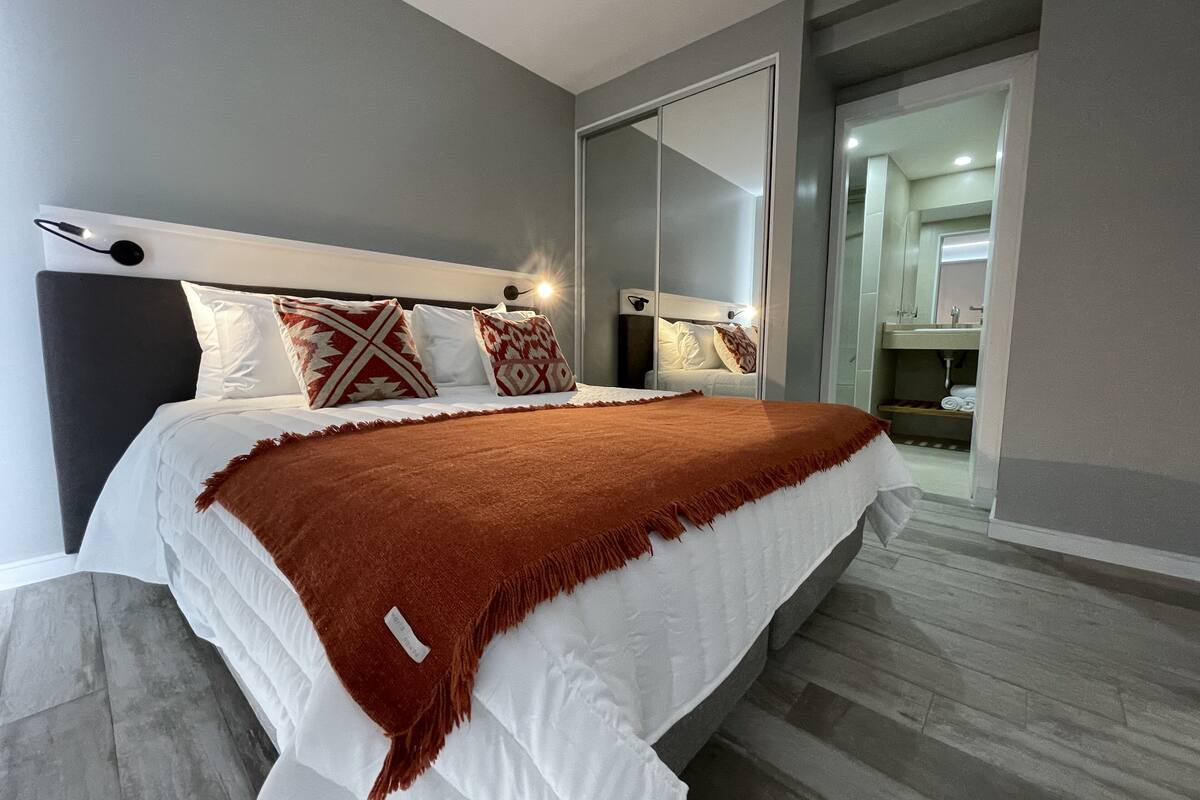 Une chambre moderne avec un grand lit, des murs gris et une porte-fenêtre coulissante donnant sur une salle de bain.