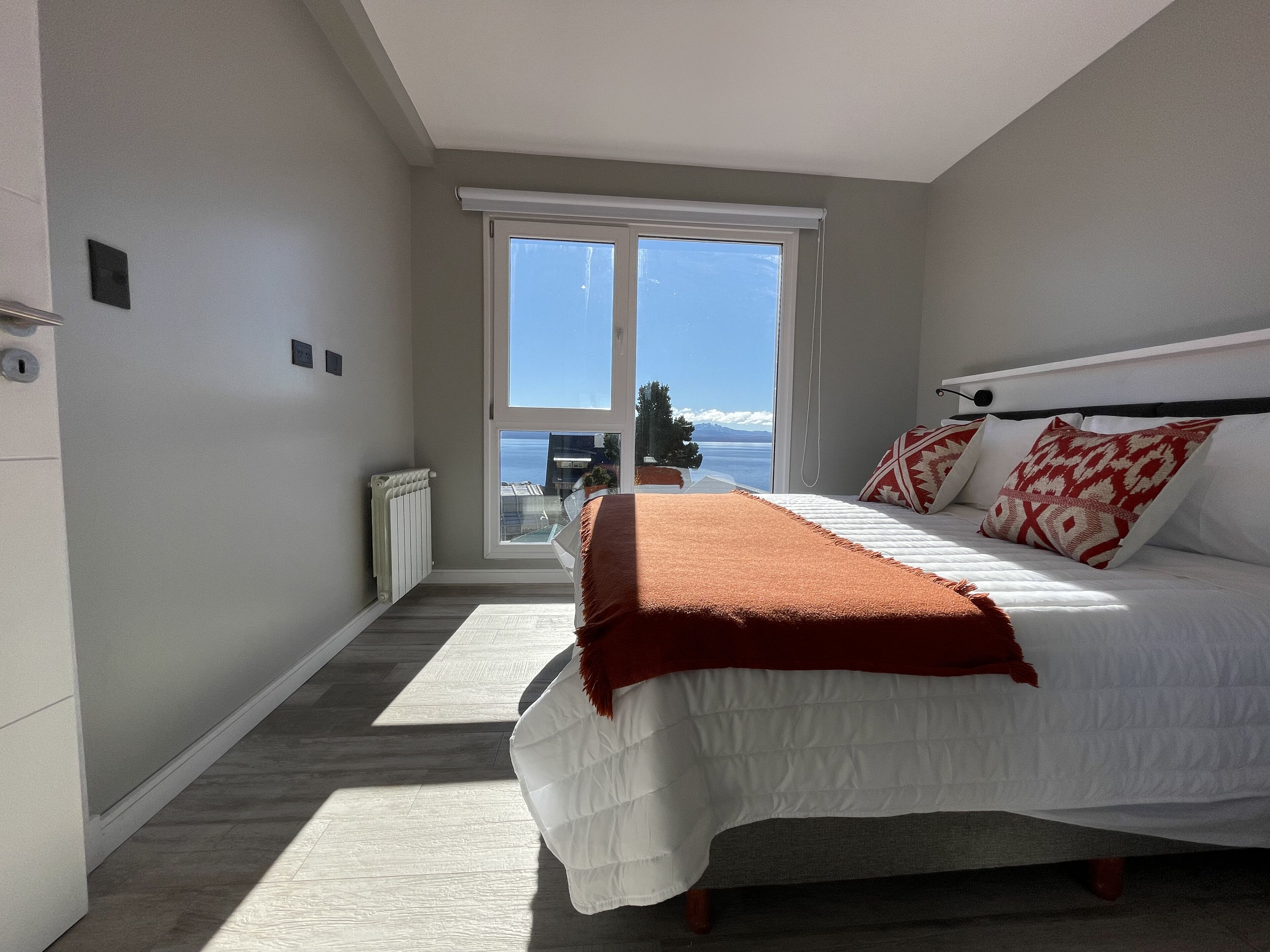 A bedroom with a bed, a window, and a view of the sea.