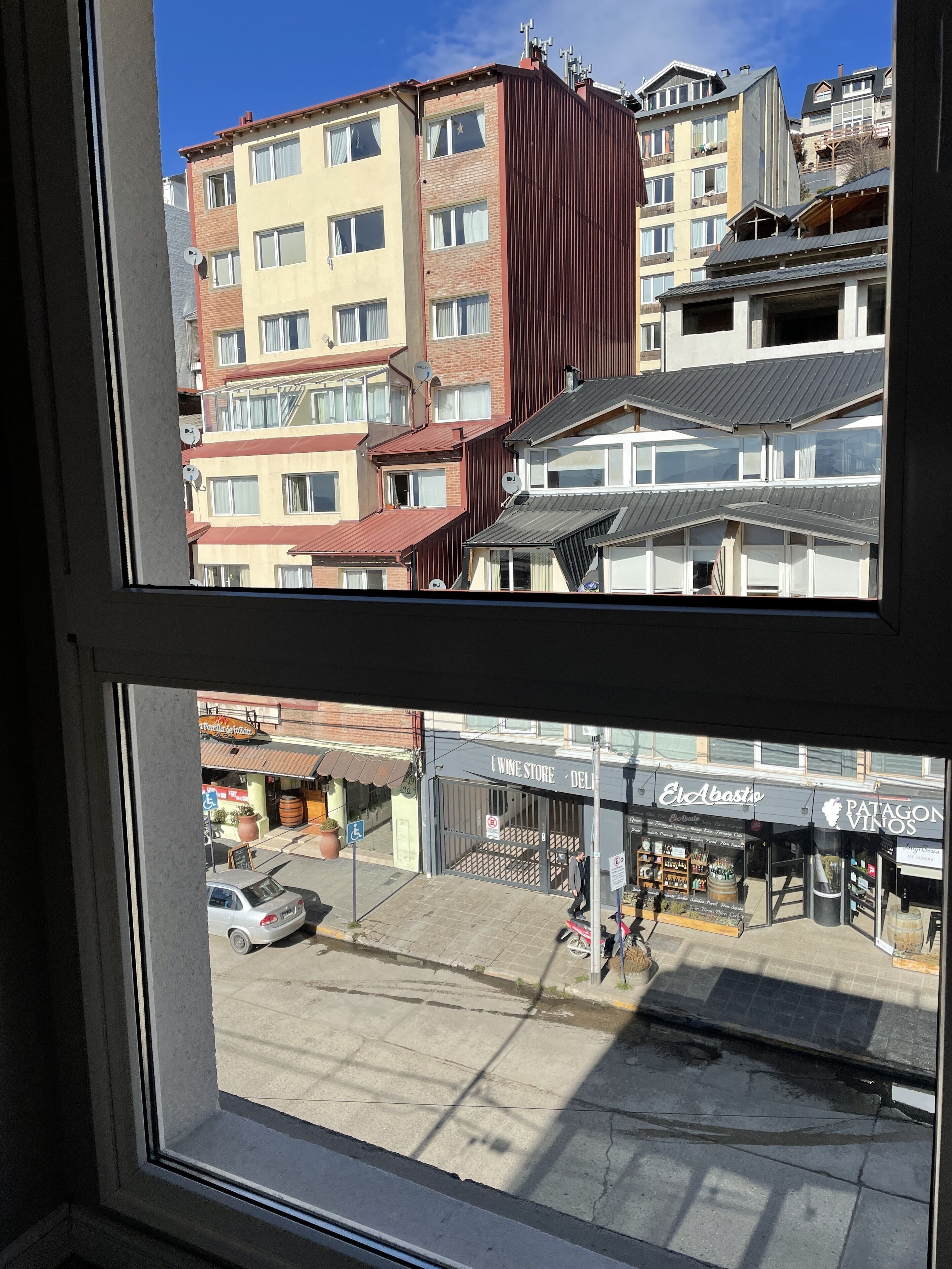 A view through a window of a multi-story building with balconies, a wine store, and a Patagon Vinos shop.