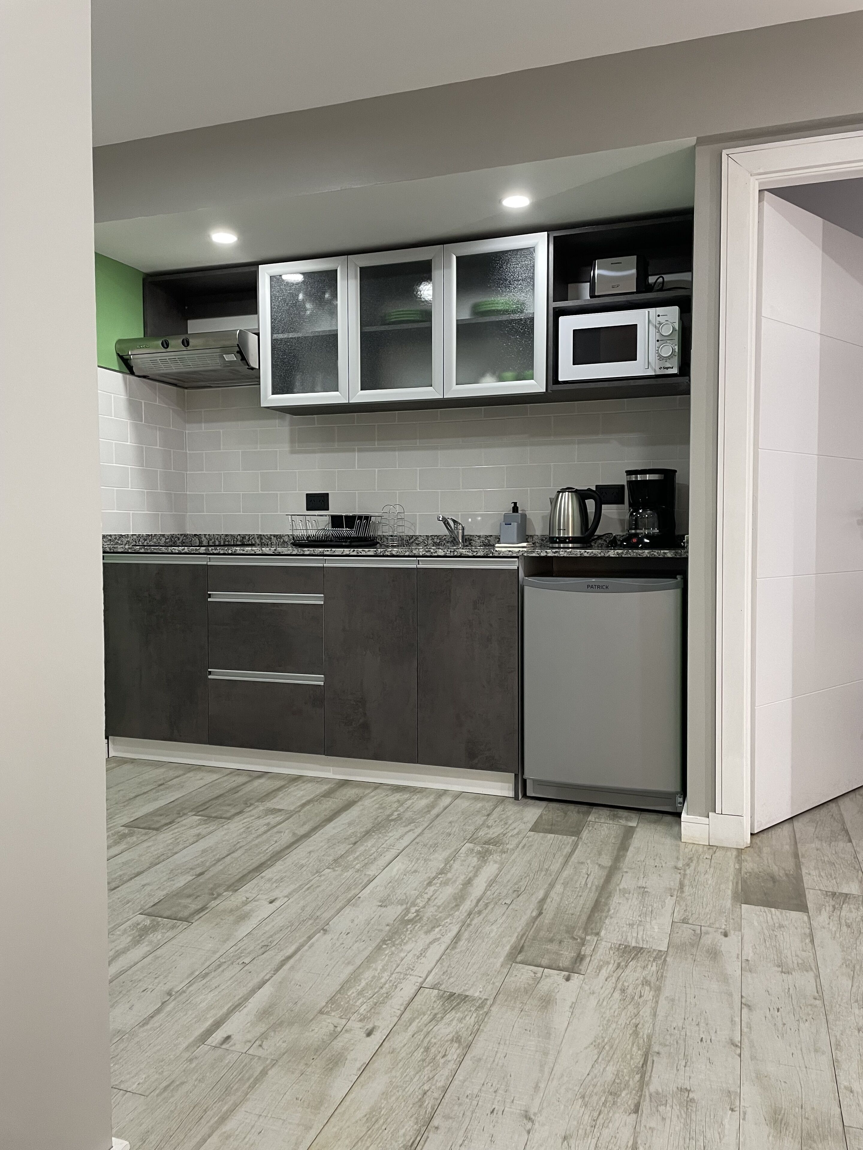 A modern kitchen with grey cabinets, a stainless steel range hood, a microwave, and a dishwasher.